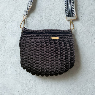 Dark textured handbag with a strap on a light gray background