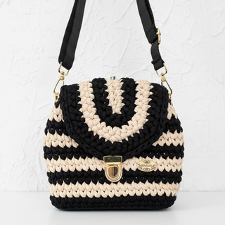 Black and beige striped handbag with a gold clasp on a textured surface.