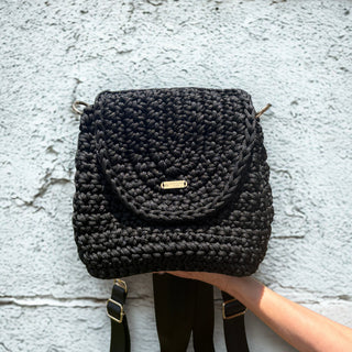 Black woven handbag held against a textured light gray wall