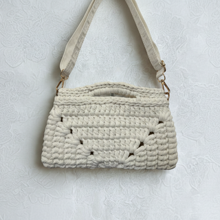 Woven beige handbag with a strap on a light textured surface.