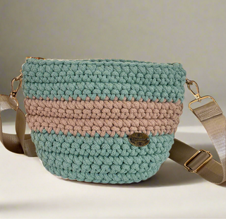 A hand-crocheted handbag with a green and brown color pattern, featuring a strap and a metallic buckle.