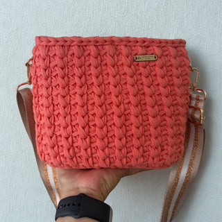 Hand holding a coral woven handbag against a light background