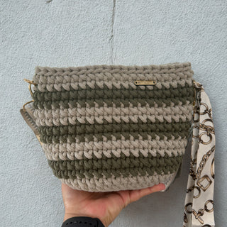 Handmade crochet bag with a patterned strap held against a light blue wall.