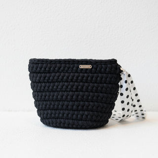 Black woven handbag with a polka dot strap on a light background