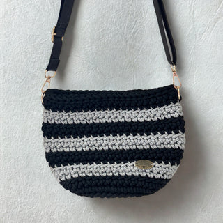 A handmade crochet crossbody bag in black and silver colors with a striped pattern, featuring a strap and a metallic clasp.