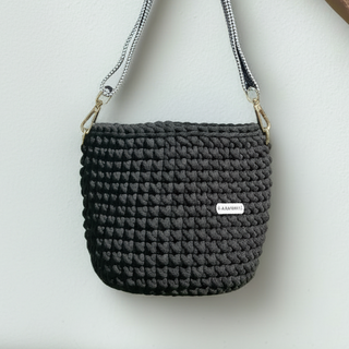 Black woven handbag with gold chain strap held by a hand on a light gray background