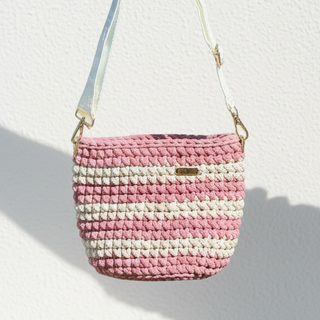 Handmade pink and white crochet bag held by a hand against a light background.