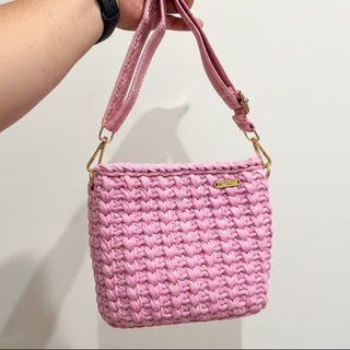 Pink woven handbag held by a person against a striped background