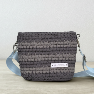 A handmade crochet crossbody bag in chocolate and caramel colors with a label showing the brand name.