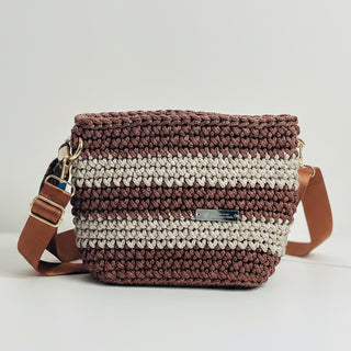 A handcrafted brown and beige striped crossbody bag with a tan strap and a metallic clasp, displayed alongside a small sunflower.