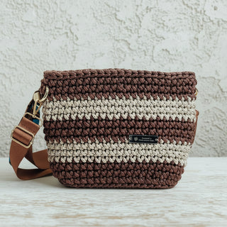 Handmade crochet crossbody bag in copper and latte colors, with a brown strap, displayed on a wooden surface.