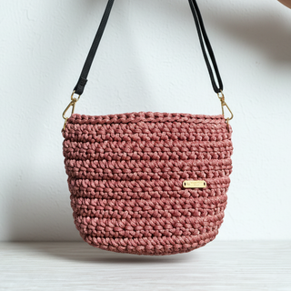 Pink crochet handbag with a gold tag on a white background