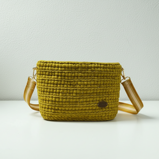 A handmade crochet crossbody bag in a golden lime color, with a gold chain strap.