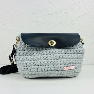A gray hand-crocheted handbag with a leather flap, displayed against a white background.