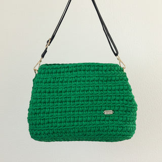 Green crocheted handbag with a black strap on a light beige background