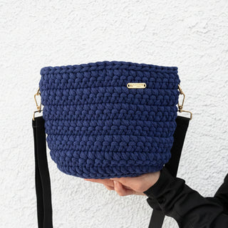 Blue knitted handbag held by a person against a white background