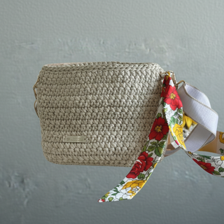 Handcrafted ivory-colored crochet crossbody bag with a floral patterned strap, displayed against a neutral background.