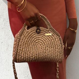 Woman in a rust-colored dress holding a crochet handbag against a light background