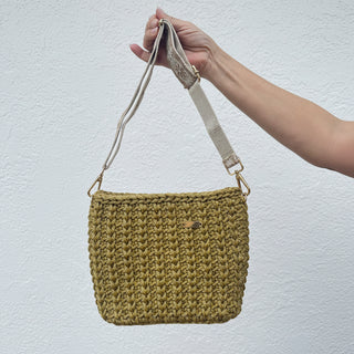 Hand holding a gold woven pouch with a blurred outdoor background
