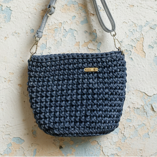 Blue crochet handbag with a strap on a textured beige surface