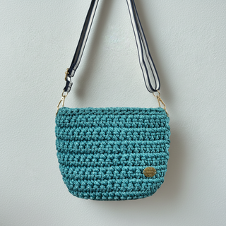 Teal crochet bag with a strap on a neutral background