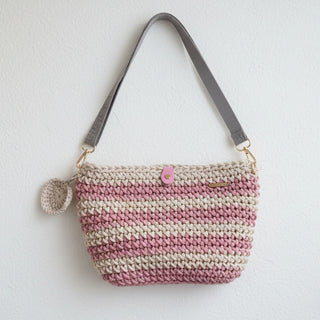 Crocheted handbag with pink and beige stripes on a textured surface with flowers.