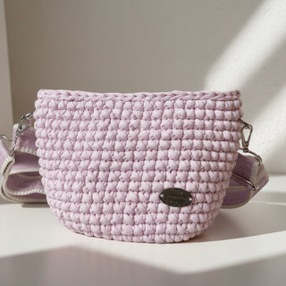 A small, pink handmade crochet crossbody bag with a tag visible on the side.