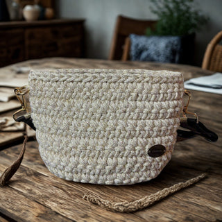 A hand-crocheted, shiny ivory handbag positioned on a wooden table with a keychain attached to it.