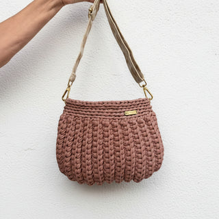Brown woven handbag with a strap held by a hand against a pink background