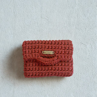 Red woven clutch bag with a brand label on a light gray background