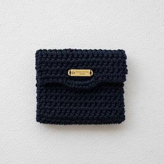 Navy blue crocheted pouch with a gold tag on a light gray background