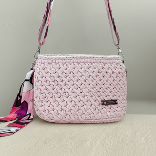 Pink woven handbag with a colorful scarf and flower decoration on a light surface.