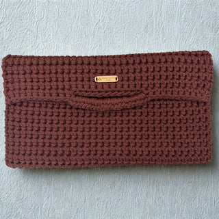 Brown crochet clutch bag with a gold tag on a light gray background