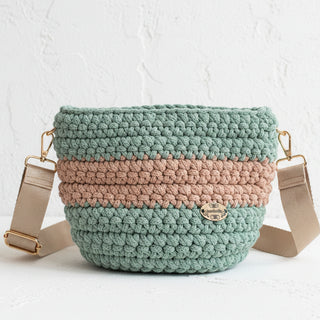 Handmade crochet crossbody bag in aloe green and caramel brown colors with a striped pattern, featuring a strap and a brand tag.