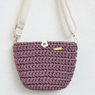 Purple crocheted handbag with beige strap on a textured surface