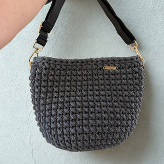 Gray textured handbag with black strap on a light blue background