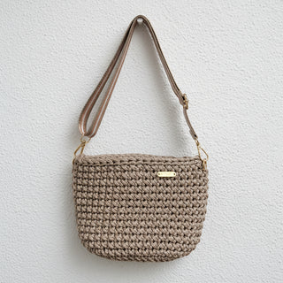 Crocheted handbag with a gold tag on a textured surface with white flowers.