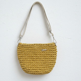 Yellow crocheted handbag with a visible brand label on a textured surface