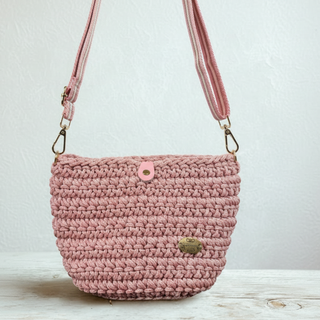 Pink crochet handbag on a wooden surface with a light background