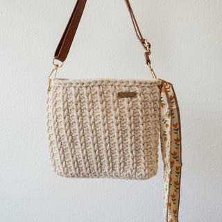 Beige textured handbag with floral strap held by a person indoors.