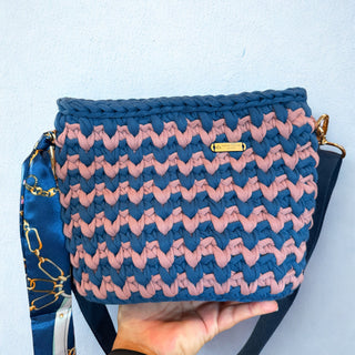 Handheld blue and pink woven clutch bag with a visible brand label on a light blue background.