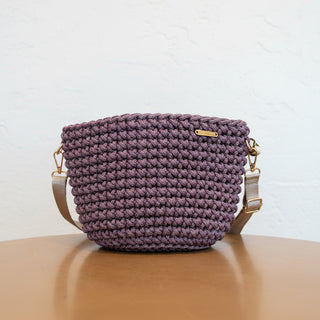 Purple crocheted bag with gold accents on a wooden surface and light background