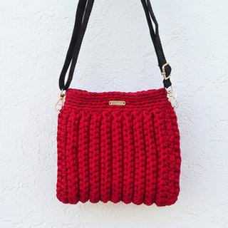 Red crochet handbag with a gold clasp on a textured wall.