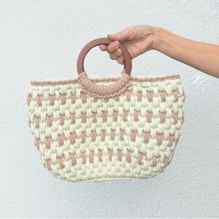 Woven handbag with pink handles held by a hand on a light surface.