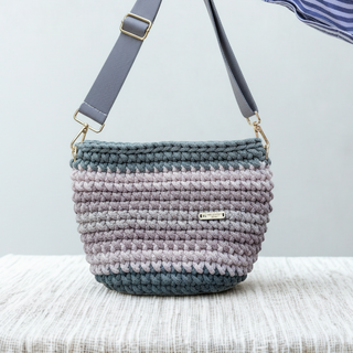 Handmade crochet bag with a gradient pattern held by a person against a neutral background