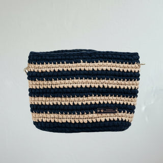 A handmade crochet crossbody bag in sapphire blue and caramel, displayed on a beige textured surface.