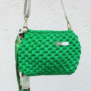 Handmade crochet crossbody bag in a nature-inspired green hue with a visible brand tag, showcasing its textured surface and a crossbody strap.